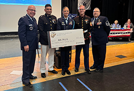 A JROTC cadet stands with instructors and a big check